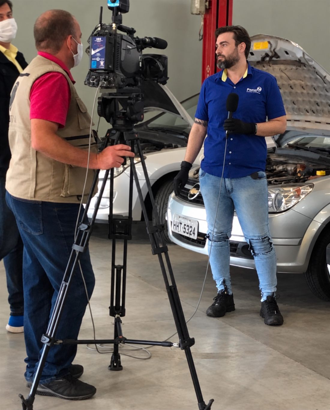 André dando entrevista dentro de um centro automotivo, ao lado de um veículo em manutenção